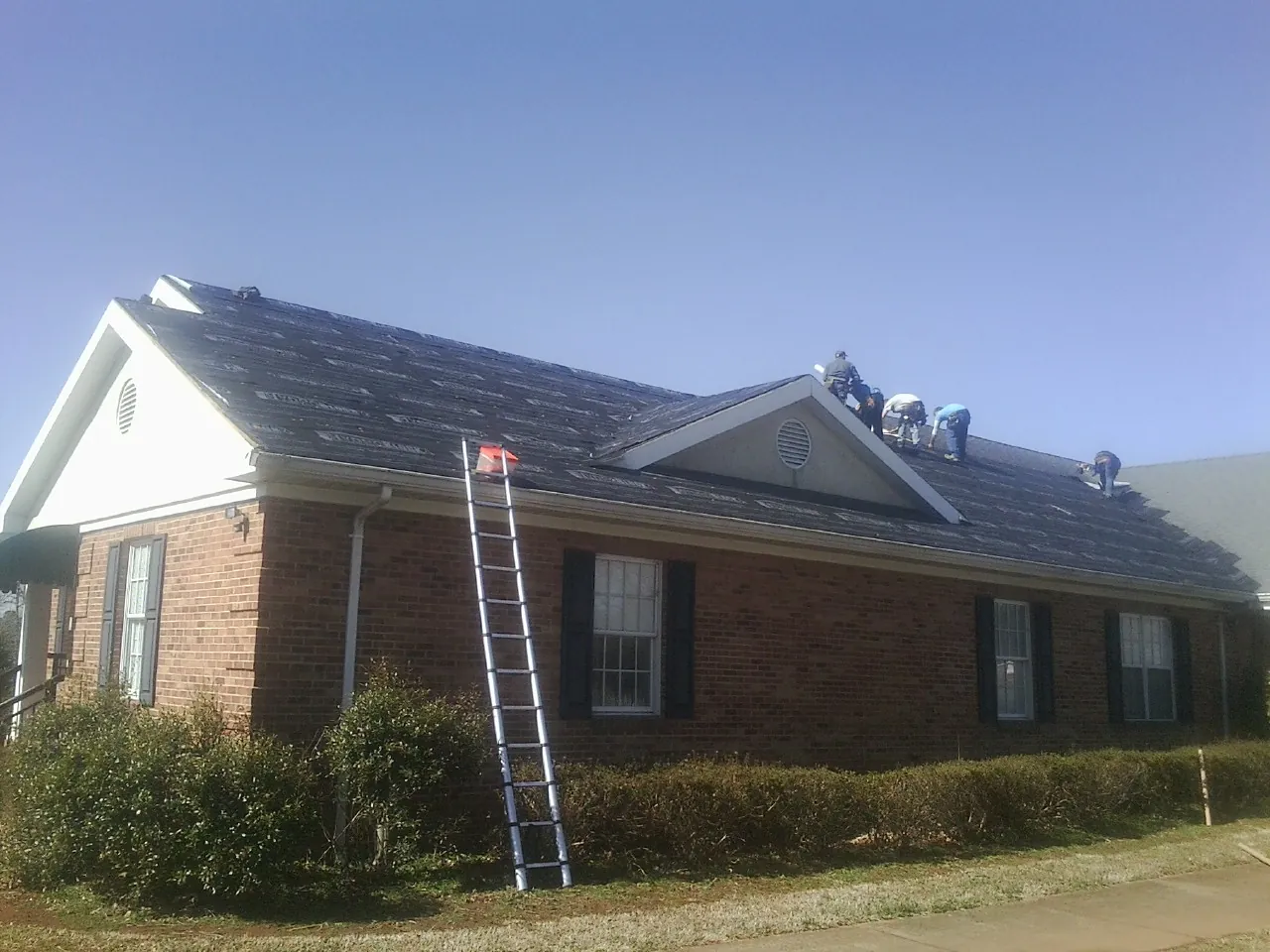 Crew tearing shingles off a brick ranch roof with a ladder set — Emergency Roof Repair work by our crew in Florissant