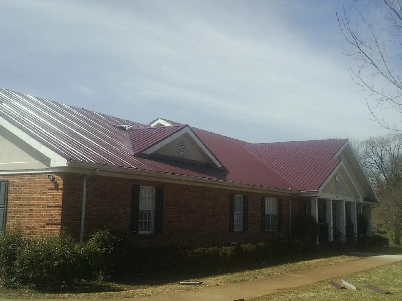 Red metal roof with gabled entries on a long brick building, from a Hail Damage Roof Repair job in Florissant