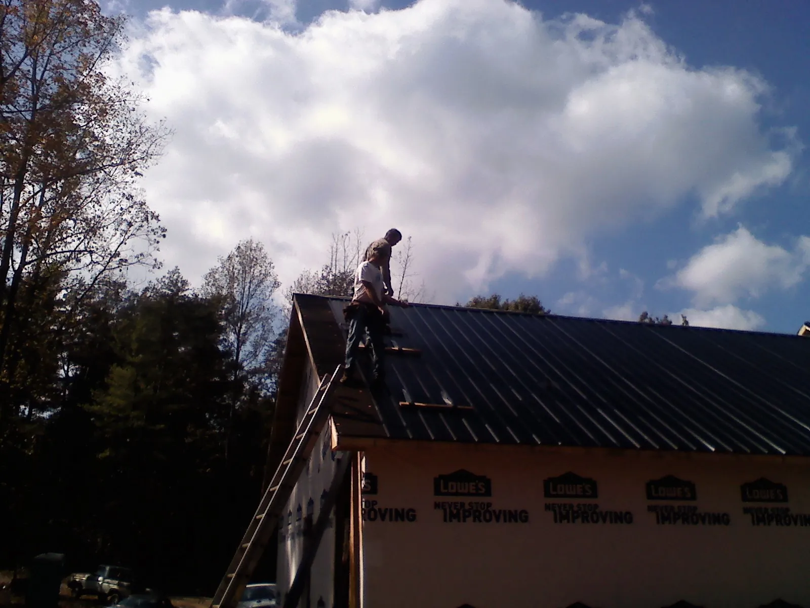 Roofer fastening dark metal panels high against a cloudy sky, from a Roof Inspection job in Florissant