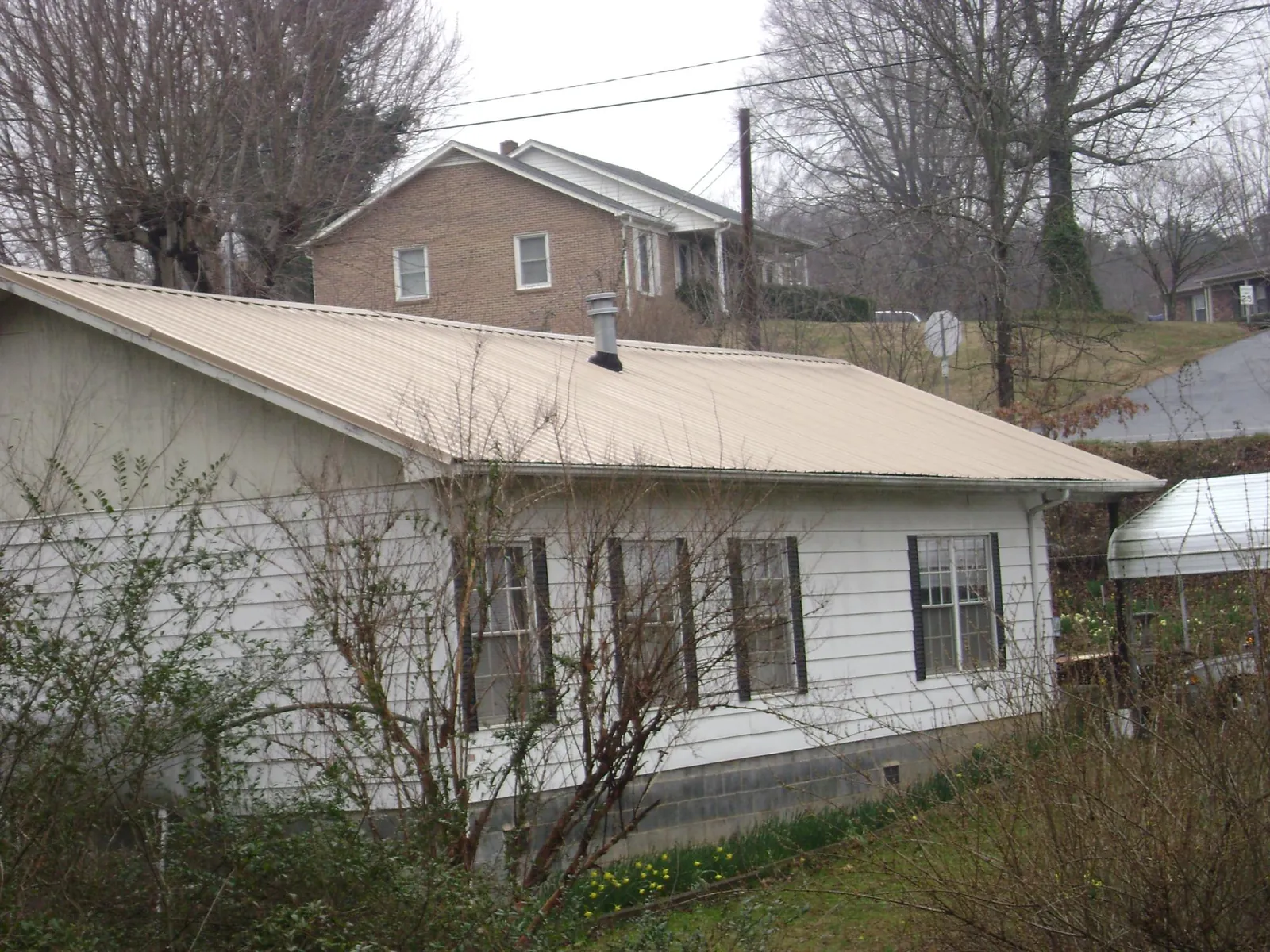 Tan metal roof on a white sided house set into a hillside — Commercial Roofing by Roofing Brothers in Florissant